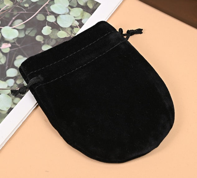 Black velvet drawstring pouch on a beige surface with a leafy background