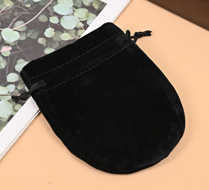 Black velvet drawstring pouch on a beige surface with a leafy background